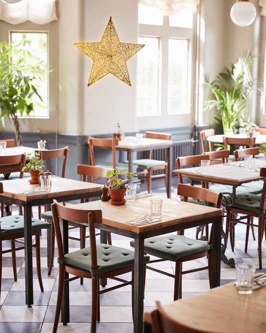 Goldener Weihnachtsstern von Alganic als Lichtobjekt in einem hellen Gastraum – dezente Festlichkeit für Hotellerie und Gastronomie.