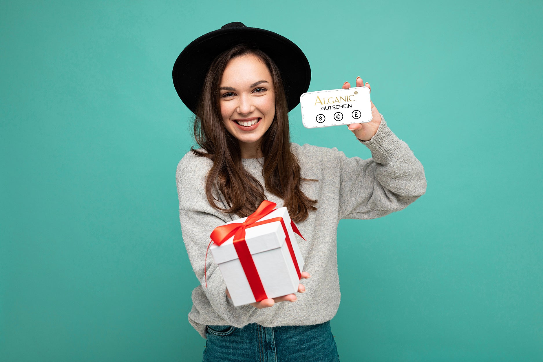 Smiling woman holding an Alganic gift card and a white present with red ribbon in front of a teal background