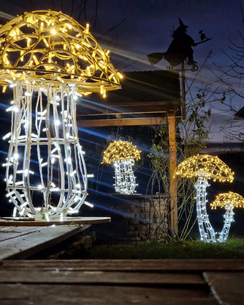 Leuchtende Pilzskulpturen aus gold-weißer Drahtstruktur als Lichtobjekte im nächtlichen Garten – inszeniert mit magischer Atmosphäre.